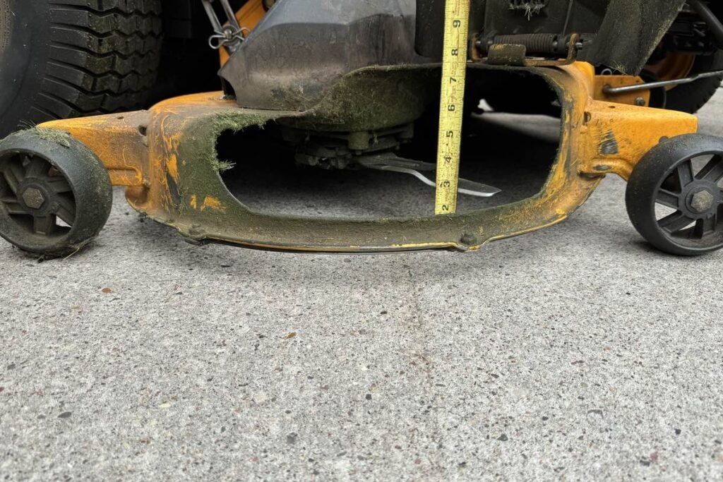 Tape measure on concrete beside a mower blade tip, showing the actual cutting height