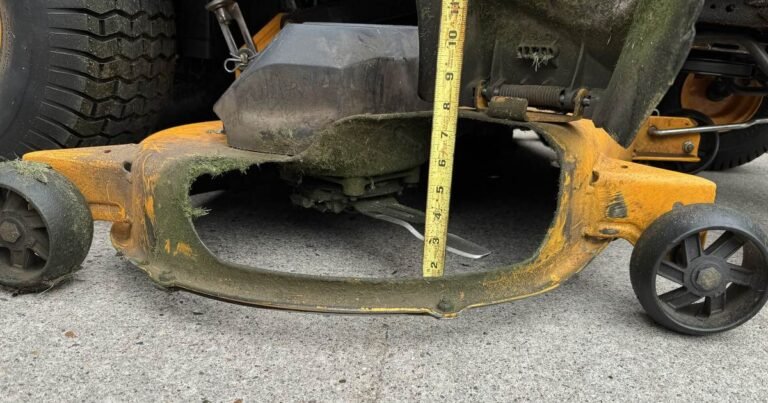 Riding mower deck with a tape measure checking cutting height on a driveway
